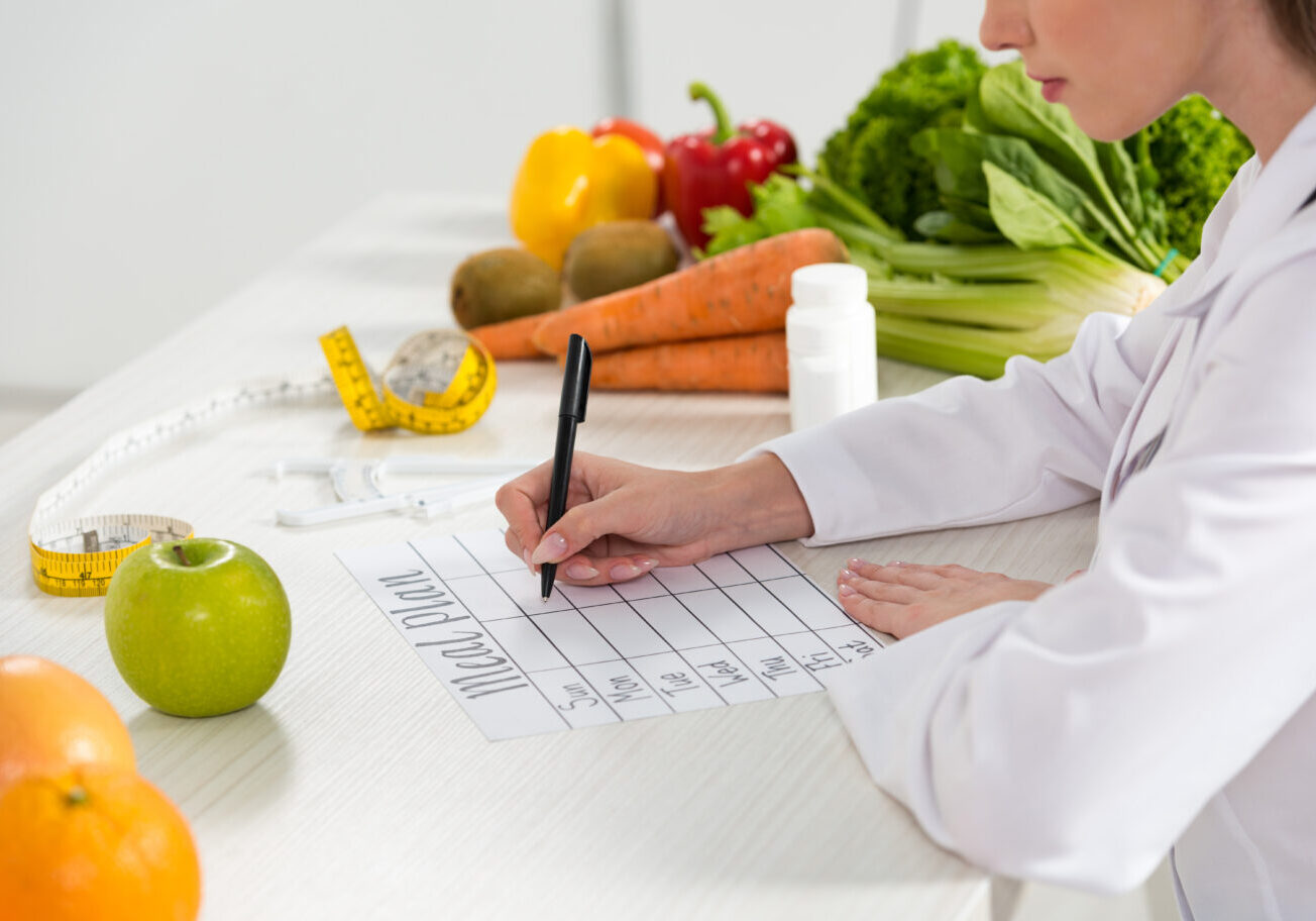 cropped view of dietitian writing in meal plan at workplace