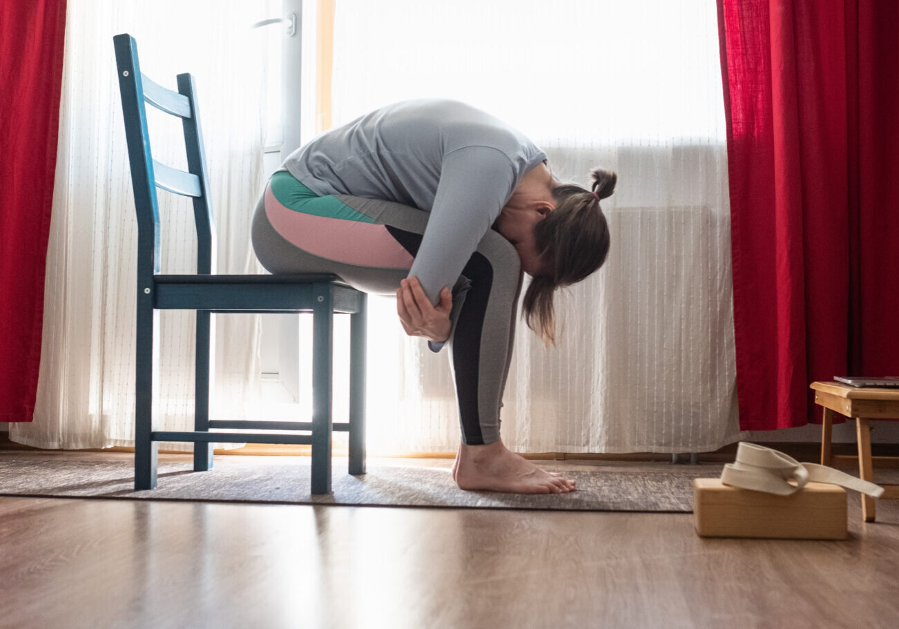 young woman in relaxing yoga pose called balasana or child pose sitting on chair in the living room.